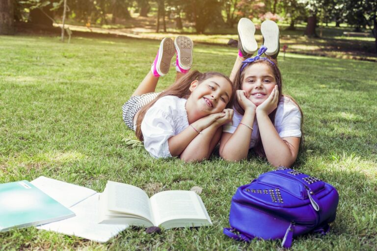 two schoolgirls lying grass with heads propped hands smiling 23 2147879235